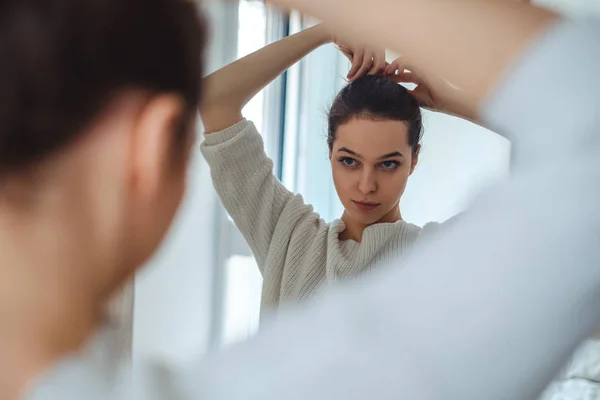 Girl looking in the mirror while making ponytail — Stock Photo, Image