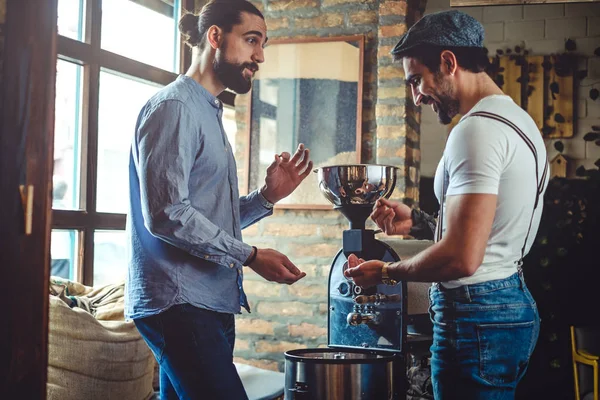 Propietarios masculinos mirando el grano de café por el tostador de café —  Fotos de Stock
