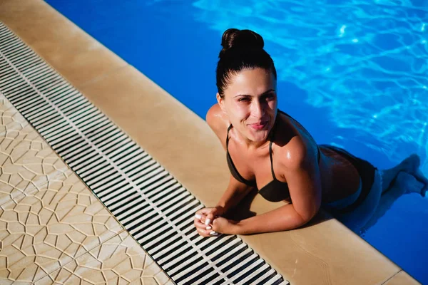 Menina sorrindo enquanto se inclina na borda da piscina — Fotografia de Stock