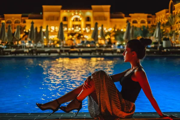 Chica sentada en el borde de la piscina por la noche —  Fotos de Stock