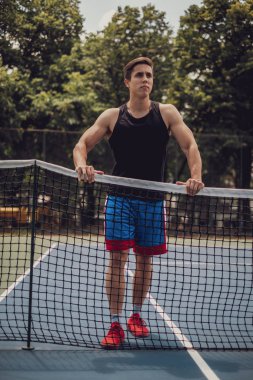 Tenis ağının önünde duran kaslı adam.