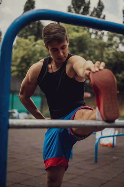 Fit muscular man stretching leg in an outdoor gym
