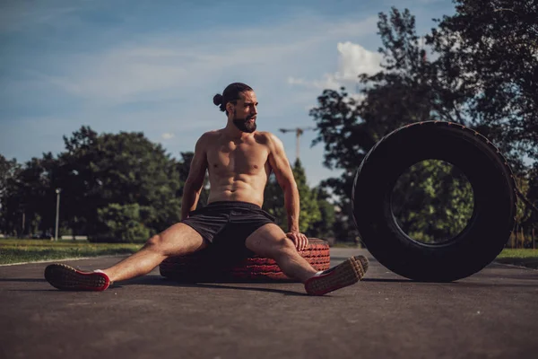 Hombre barbudo descansando sobre un neumático después del entrenamiento —  Fotos de Stock