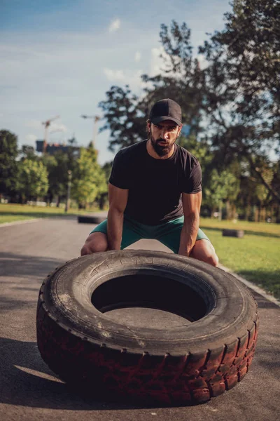 Hombre barbudo con sombrero volteando neumático en el parque —  Fotos de Stock