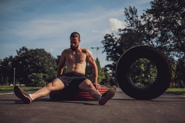 Hombre barbudo cansado sentado en un neumático después del entrenamiento —  Fotos de Stock