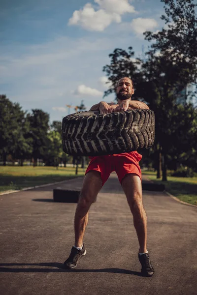 Atleta barbudo tratando de levantar neumáticos en el parque —  Fotos de Stock