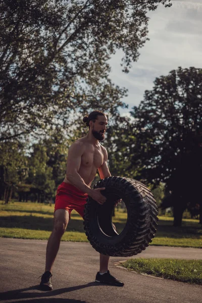 Hipster atleta tratando de levantar el neumático en el parque —  Fotos de Stock
