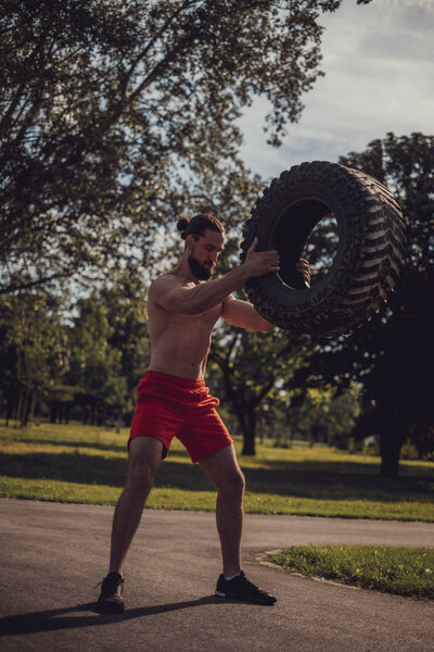 Macho athlete lifting tire in the park