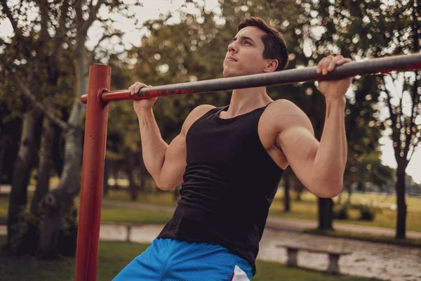 Man doing chin ups on the bar in the park — Stock Photo, Image