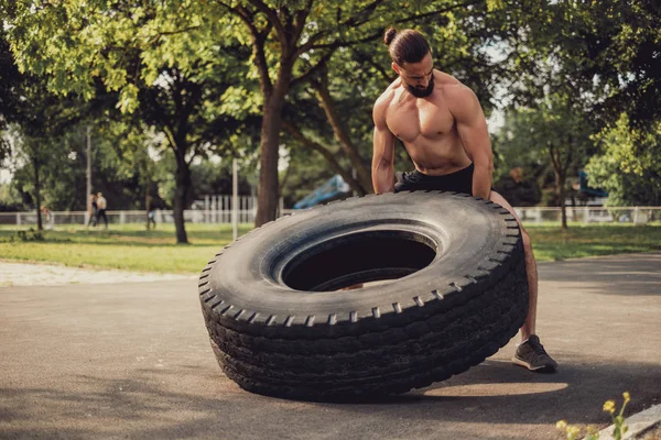 Hipster musculoso barbudo haciendo ejercicio con neumático en el parque —  Fotos de Stock