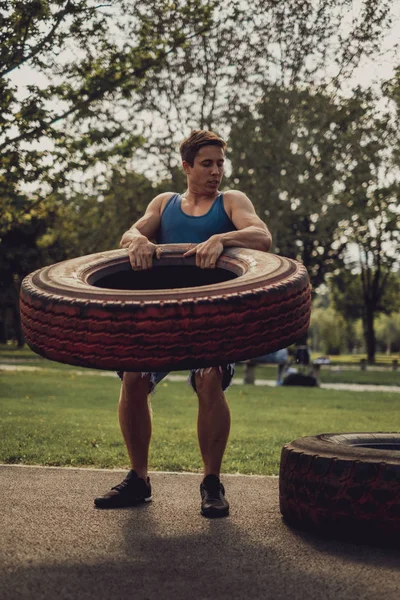 Hombre atlético levantando neumático en el parque —  Fotos de Stock