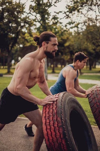 Difícil muscular homens lançando pneus no parque — Fotografia de Stock