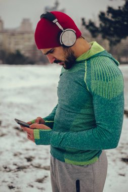 Açık havada müzik dinlerken cep telefonu kullanan bir sporcu