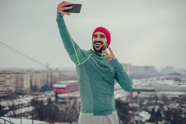 Hombre atlético sonriente tomando selfie con paisaje urbano en el backgro —  Fotos de Stock