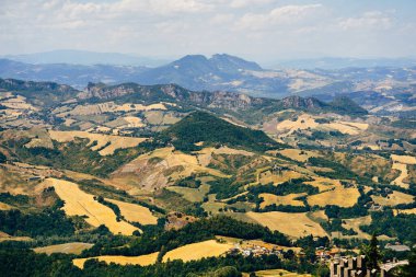 Mavi gökyüzüne karşı yeşil bitkileri olan dağlar. San Marino 'daki dağların eteklerindeki sarı tarlalar.