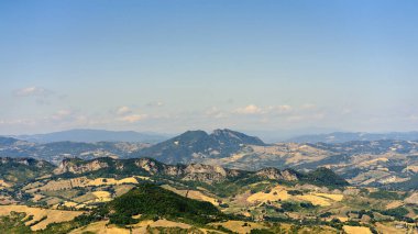 Mavi gökyüzüne karşı yeşil bitkileri olan dağlar. San Marino 'daki dağların eteklerindeki sarı tarlalar.