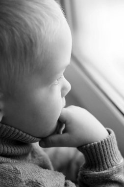 Siyah ve beyaz pencereden dışarı bakarak küçük üzgün çocuk