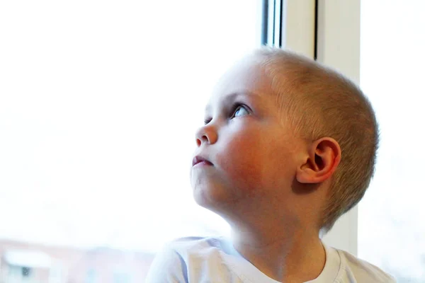 Adorable niño rubio sentado cerca de la ventana, tan triste — Foto de Stock