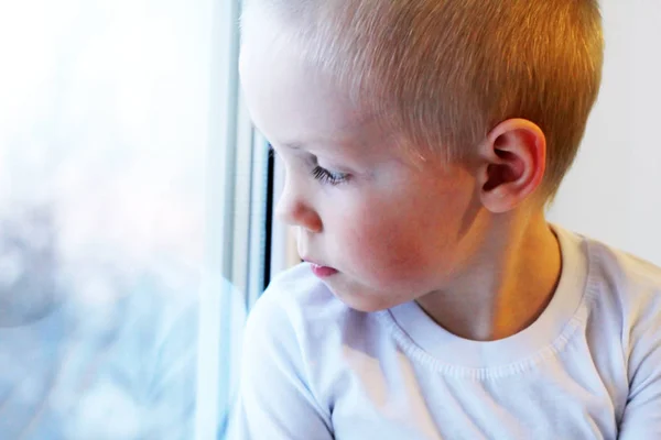 Adorable niño rubio sentado cerca de la ventana, tan triste — Foto de Stock