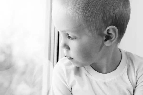 Adorable niño rubio sentado cerca de la ventana, tan triste — Foto de Stock
