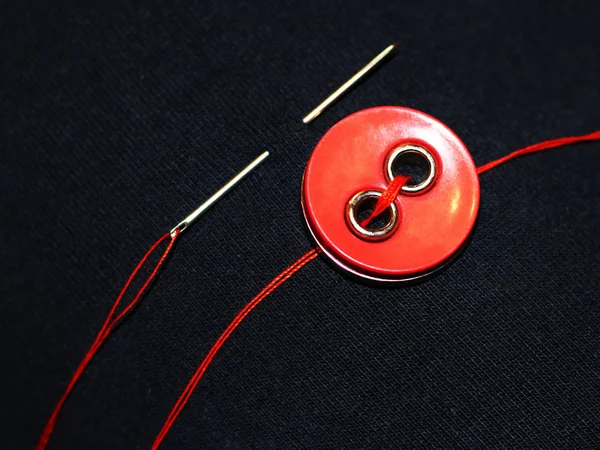Красная кнопка и игла на черной ткани — стоковое фото
