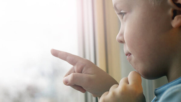 A little boy draws on the glass with his finger