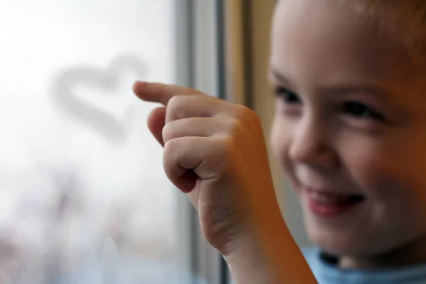 Un niño pequeño dibuja en el cristal con su dedo, corazón — Foto de Stock