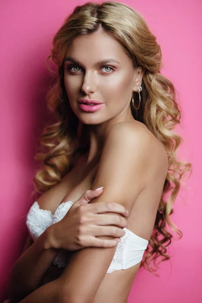 Vackra glada blond ung kvinna poserar i vita underkläder. Perfekt smal sexig kropp. Tjej med långt lockigt hår. Rosa bakgrund. Glamour makeup. — Stockfoto