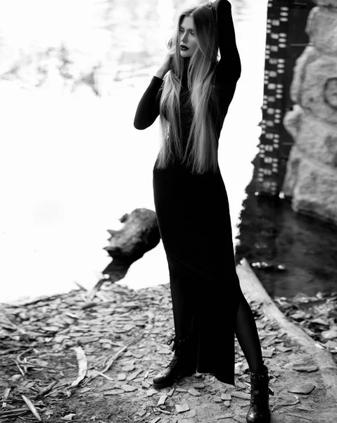 Young woman stands alone near a river with a bridge Mist over water. Foggy air. Early chilly morning. Dark, scary moment and gloomy atmosphere. Black and white photo