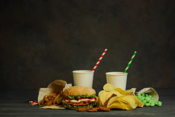 Drinks in a paper cup with a paper tube and hamburger, salty snacks, pretzels, chips.