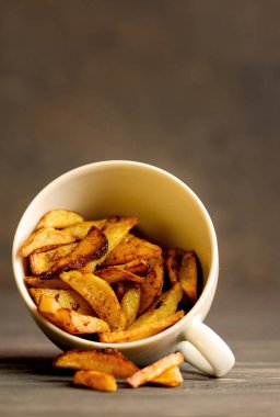 Kır usulü patates kızartması. Koyu ahşap arka planda beyaz bir fincanda patates kızartması.
