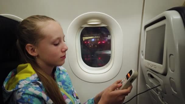 Menina segurando o controlador remoto para o sistema de entretenimento no avião . — Vídeo de Stock