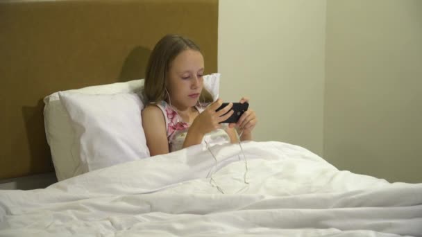 Menina na cama com um smartphone em suas mãos — Vídeo de Stock