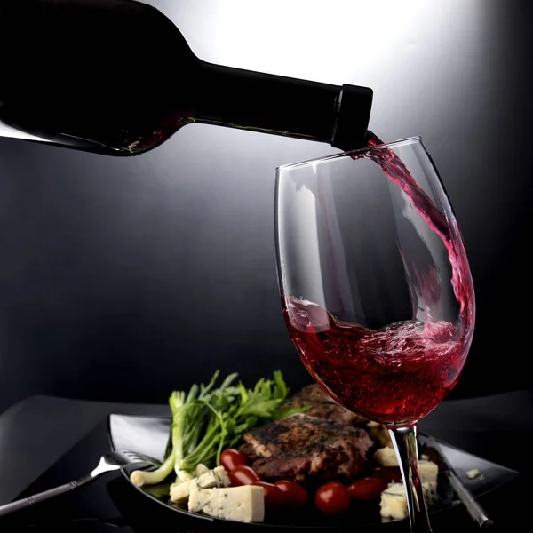 Closeup de vinho tinto derramando em um copo com queijo e carne — Fotografia de Stock