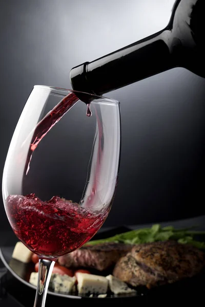 Närbild av rött vin hälla i ett glas framför plattan med ost och kött — Stockfoto