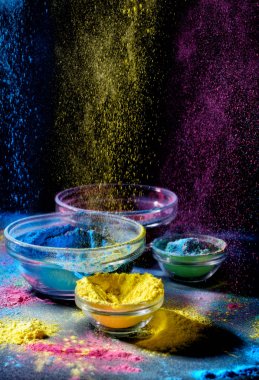 Indian Holi festival colours. Several bowls with Holi paint powder. Explosion of purple, yellow and blue color. clipart