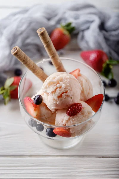 Several scoops of strawberry ice cream with wafer, strawberry and blue berry in glass against white wooden table. Summer background. View from above. — Stock Photo, Image