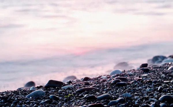 Stenen op kiezel strand en zee water bij zonsondergang. Achtergrond. Diagonaal schot. — Stockfoto