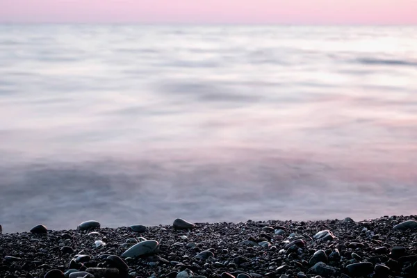 Stenen op kiezel strand en zee water bij zonsondergang. Achtergrond. — Stockfoto