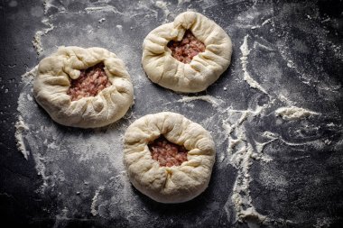 Siyah yüzeyler taze etli üç çiğ börek un ile kaplı. Üçgen formu. Hazırlık süreci.