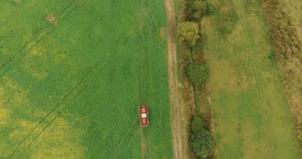 Тракторный распылитель зеленого поля возле деревенских домов осенью — стоковое видео
