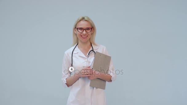 Женщина-врач в белом халате и стетоскопе улыбается, глядя в камеру — стоковое видео