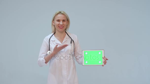 Porträtt av en kvinnlig läkare med vit päls och tablett och stetoskop leende tittar in i kameran — Stockvideo