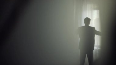 Genç adam bir takım elbise pencerenin önünde giyiyor.