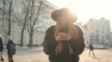 Parlak güneş ışığı altında çok güzel genç kadın telefonunu dururken şehir merkezinde kullanır.