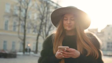 Parlak güneş ışığı altında çok güzel genç kadın telefonunu dururken şehir merkezinde kullanır.