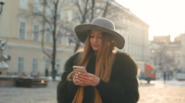 Esmer kadın kalabalık şehir sokak ayakta ve mesaj attığın için telefonunu kullanarak gri şapkalı