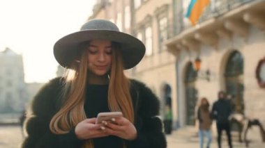 Gri şapkalı kalabalık şehir sokak ayakta ve mesaj attığın için telefonunu kullanarak muhteşem bir esmer kadın
