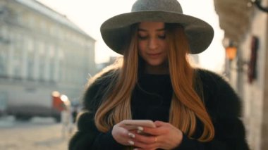 Parlak güneş ışığı altında çok güzel genç kadın telefonunu dururken şehir merkezinde kullanır.