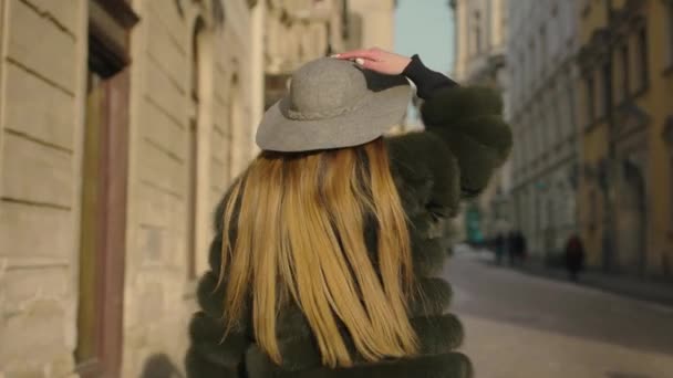 Mujer joven con el pelo largo, grandes ojos azules en un gris se precipita en el centro de la ciudad, que se vuelve a la cámara y sonríe — Vídeos de Stock